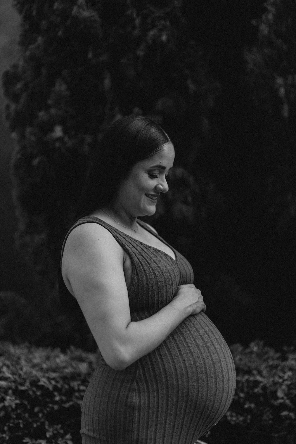 Black and white maternity photos showing an expectant mother in a ribbed dress against a dark background.
