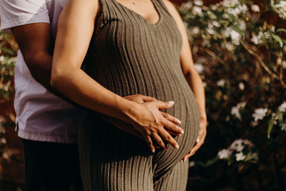 A series of maternity photos showing a pregnant belly in a brown dress against a sunlit outdoor backdrop.