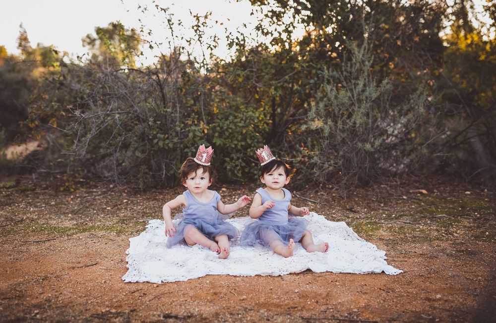 Two children sitting together on a white blanket in a wooded outdoor setting during fall.