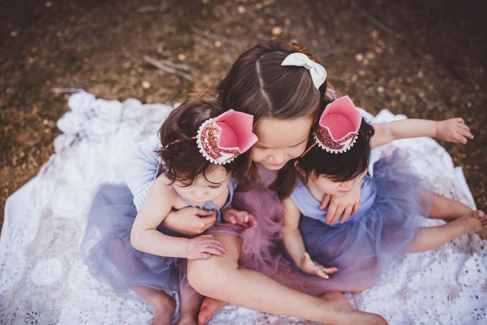 Family lying together on a white blanket outdoors sharing tender moments during a photo session.