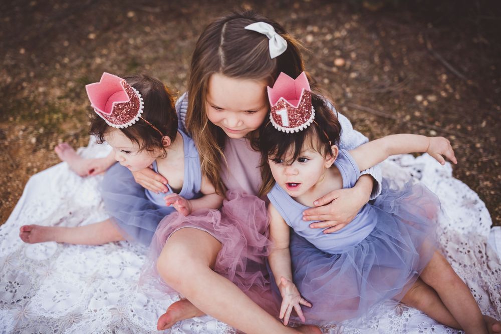 Children in tulle dresses pose together on a white blanket during an outdoor photoshoot.
