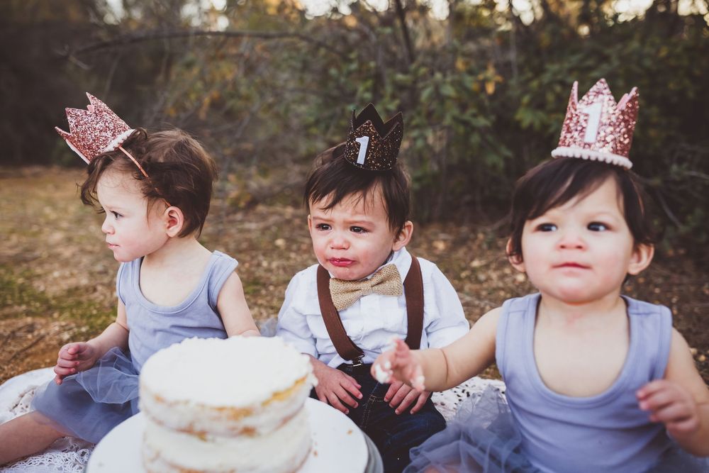 Two children in matching purple outfits share a cake during an outdoor cake smash photography session.