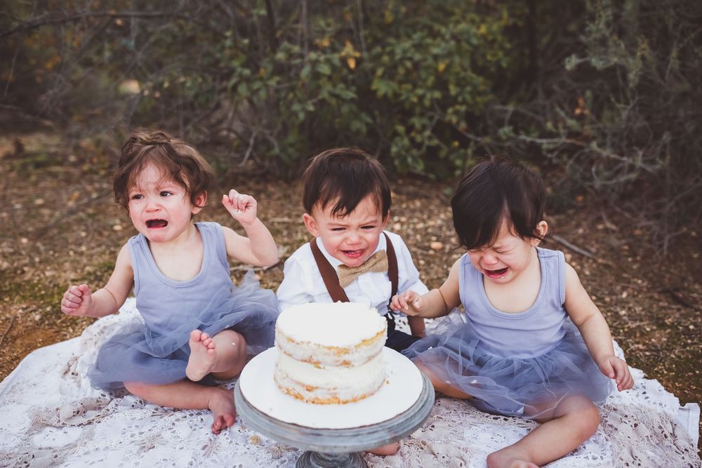 Children celebrating with cake on a white blanket during an outdoor autumn photoshoot.