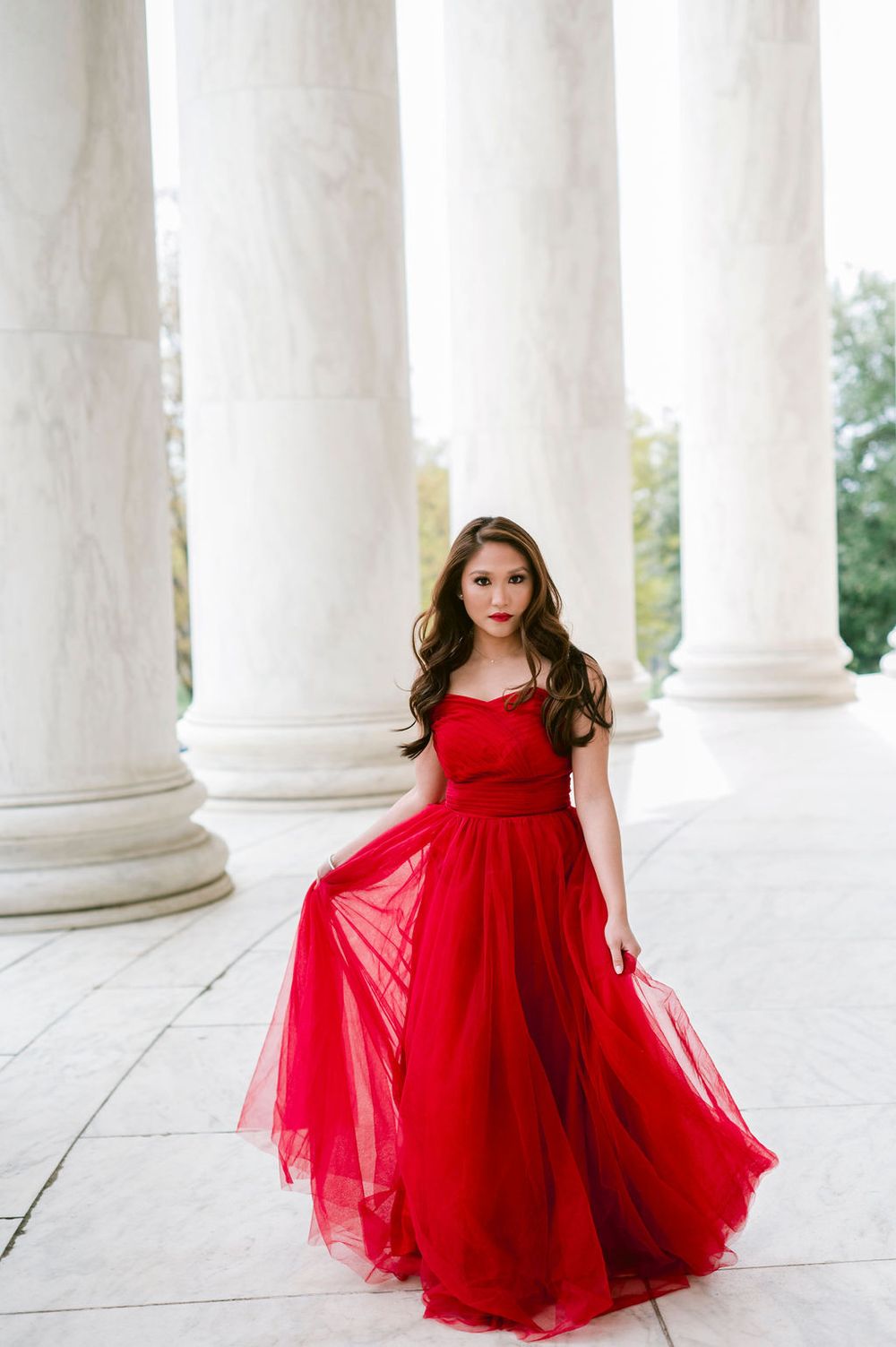 A flowing red gown twirls gracefully among white classical columns in an outdoor setting.
