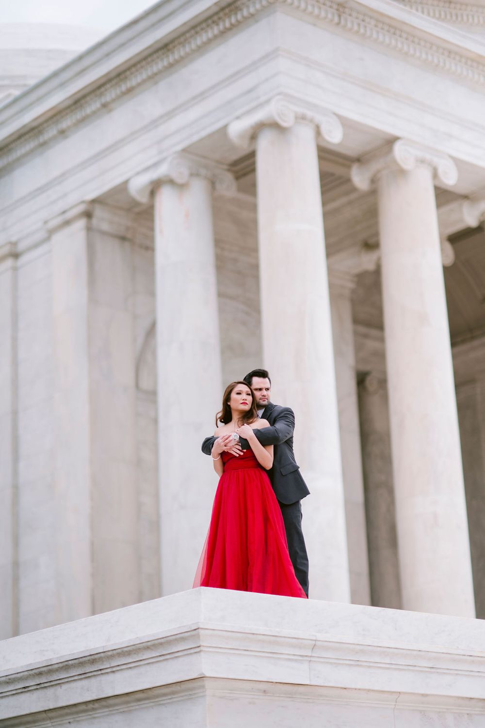 A romantic couple in formal wear embraces against white marble columns at the Jefferson Memorial in Washington DC.