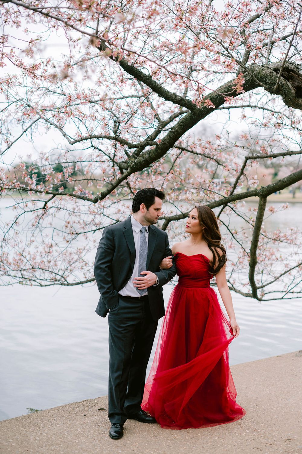 A romantic photoshoot under cherry blossom trees with a red dress and dark suit.