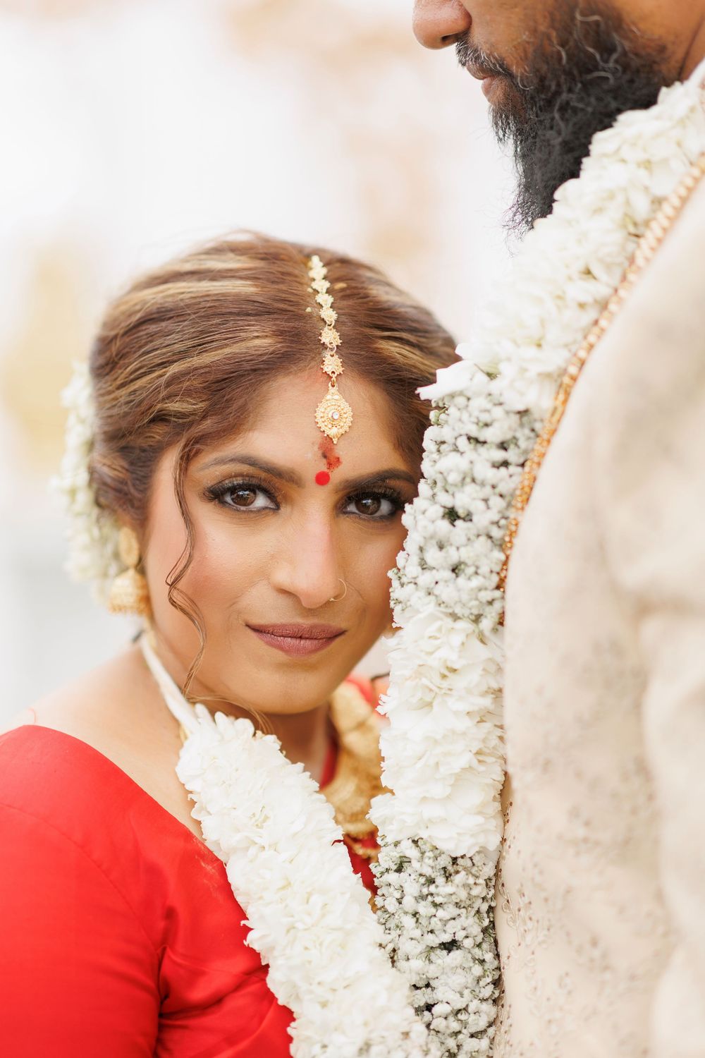 Traditional Indian wedding ceremony with white floral decor and couple in red and cream attire.