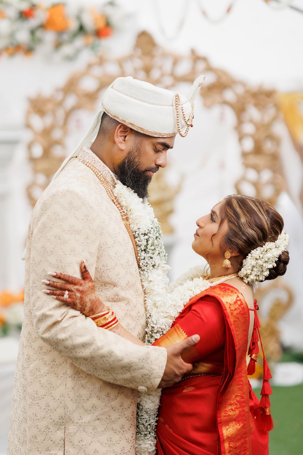 A couple in traditional wedding attire embraces during their multicultural ceremony with floral decorations.