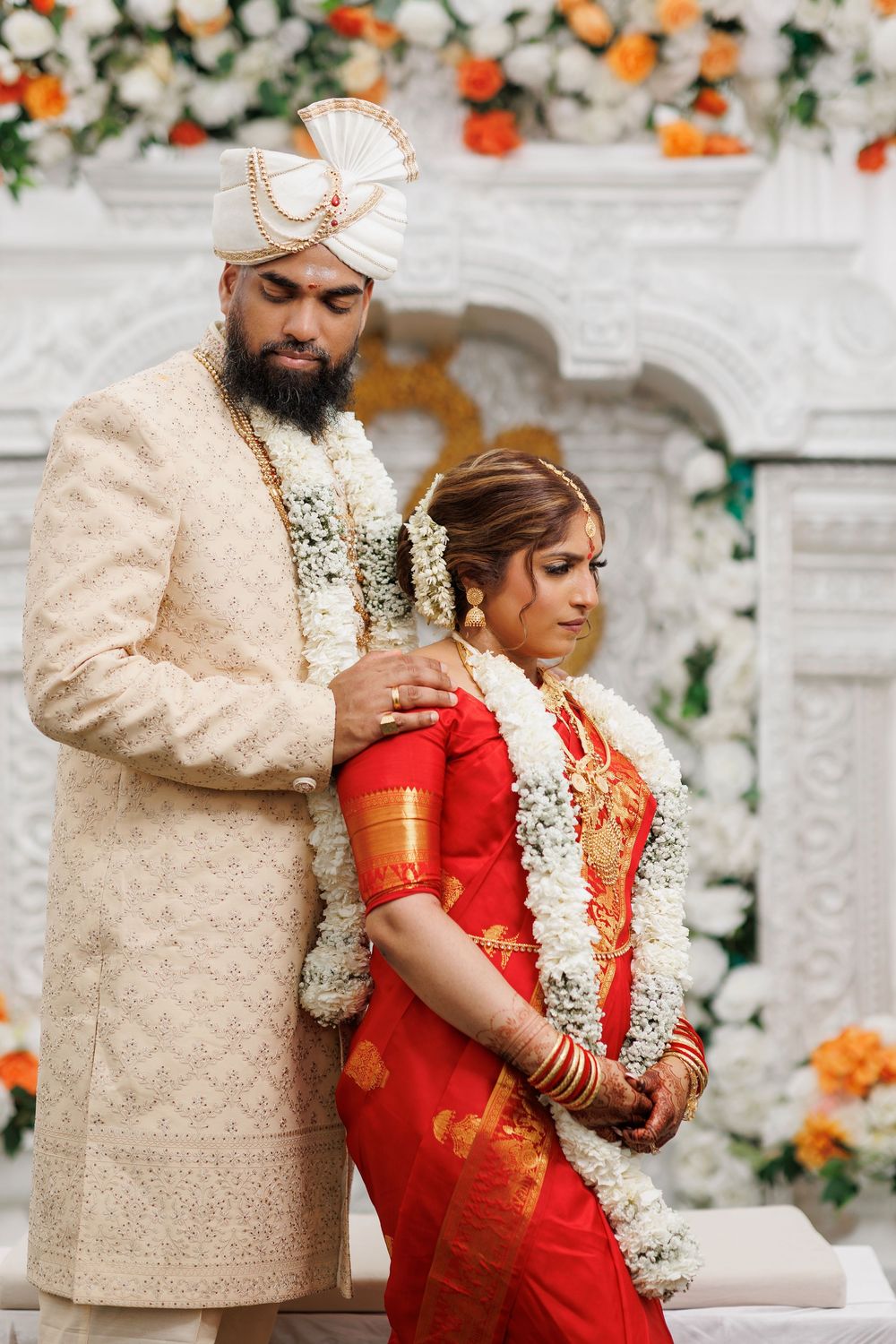 Intimate wedding moment with couple in traditional Indian attire against floral backdrop.