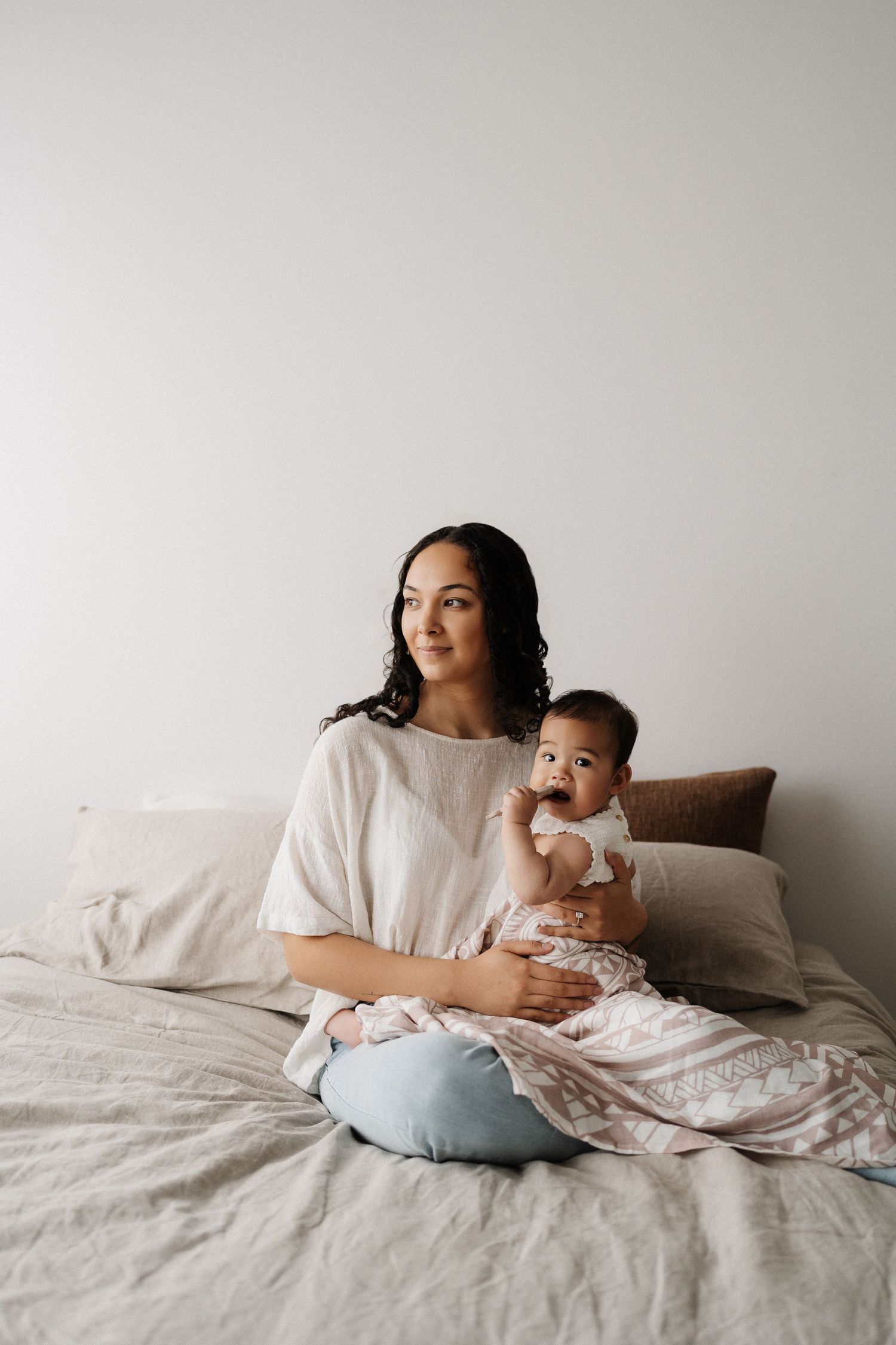A series of intimate lifestyle photos showing a parent and baby relaxing together on a white bed.