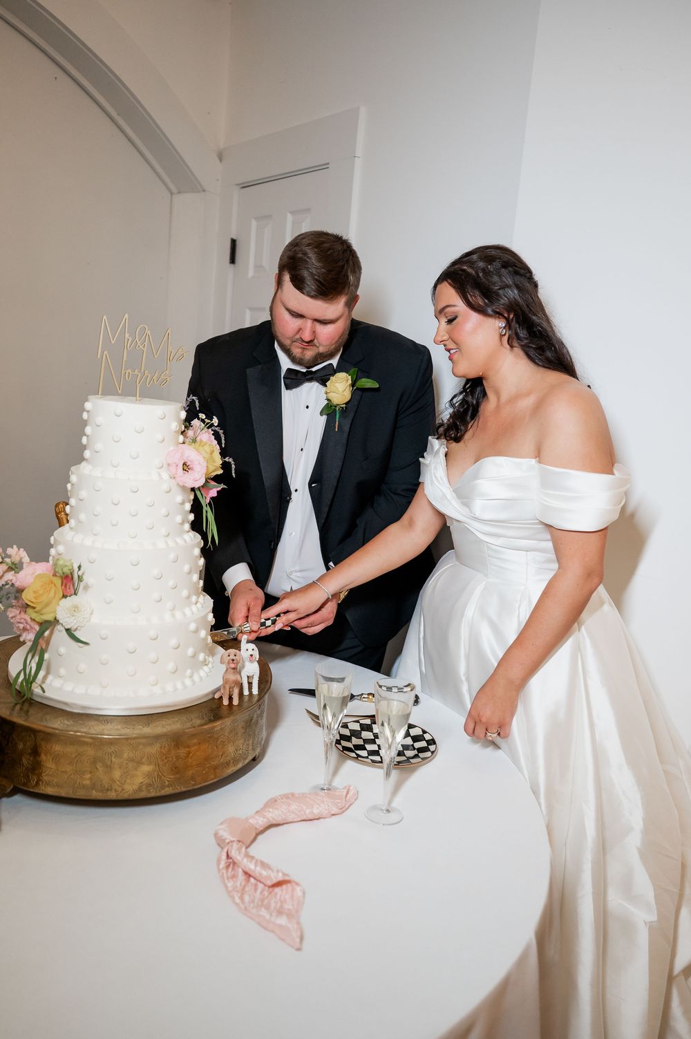 A wedding couple cuts into their elegant white tiered cake decorated with fresh flowers.