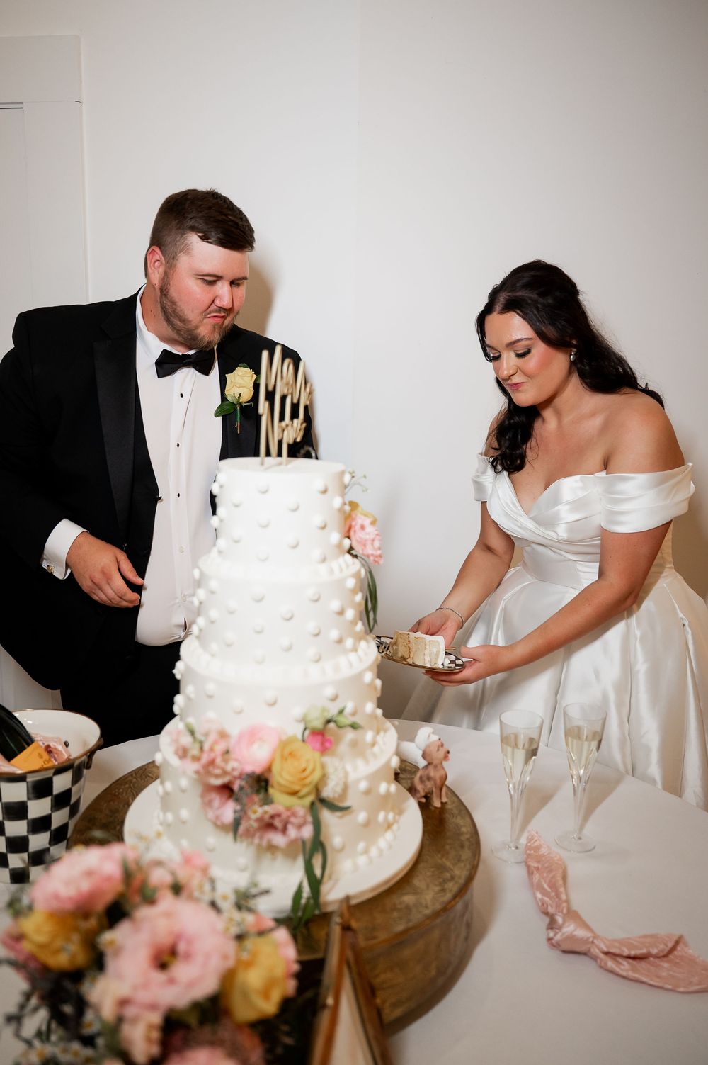 A couple cuts their elegant white wedding cake decorated with floral accents at their reception.