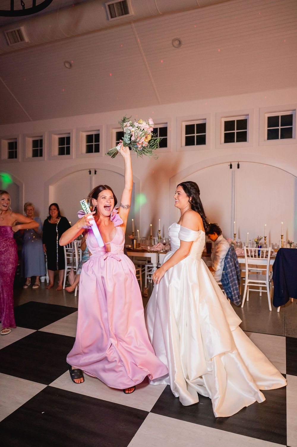 Two wedding guests in elegant gowns celebrate on a black and white dance floor.
