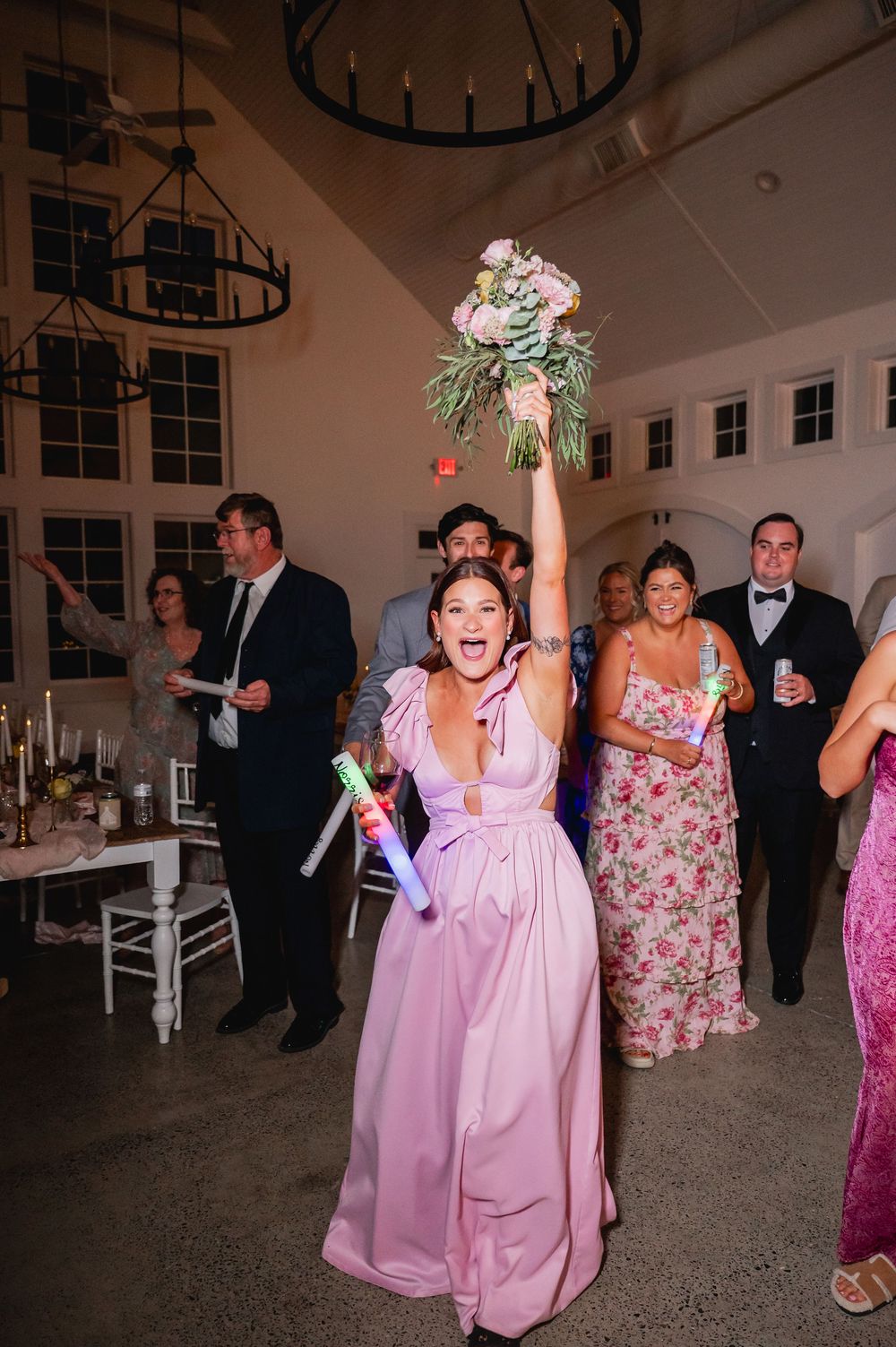 Wedding guest in pink gown enthusiastically catches the bridal bouquet during reception.