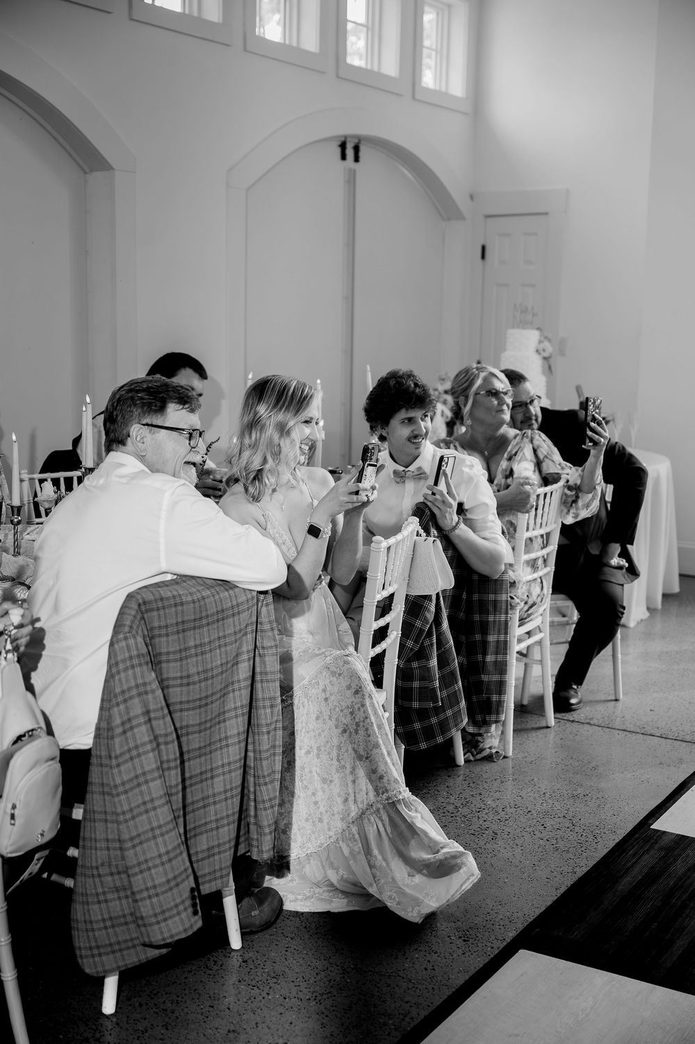 Black and white photo of wedding guests seated at tables enjoying the reception celebration.