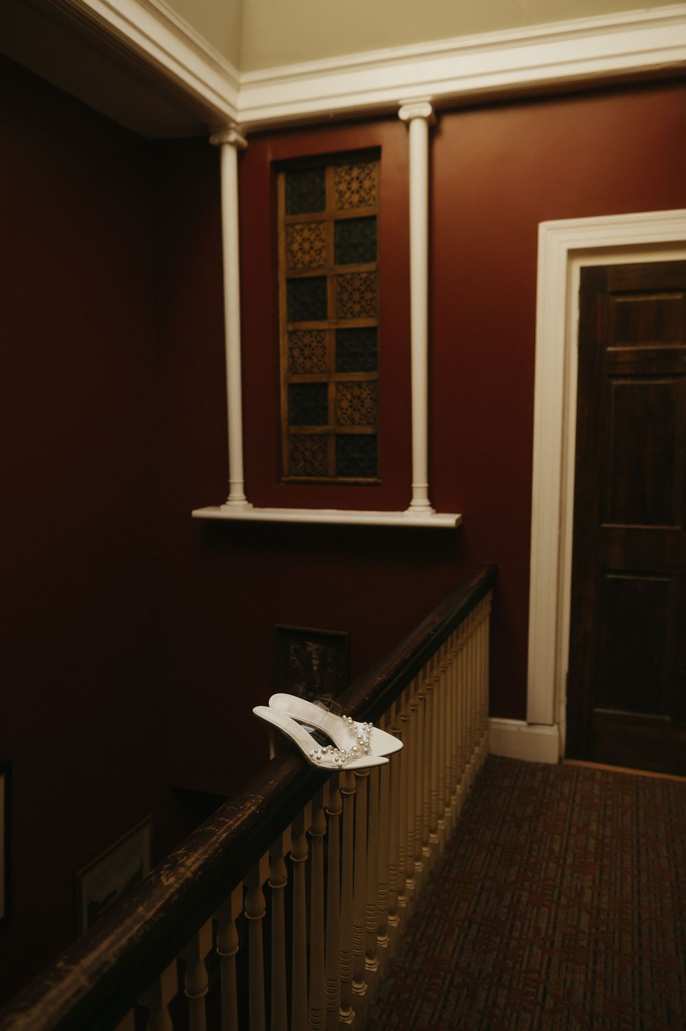 Dark hallway interior with wooden staircase and decorative stained glass window in classic architectural style.