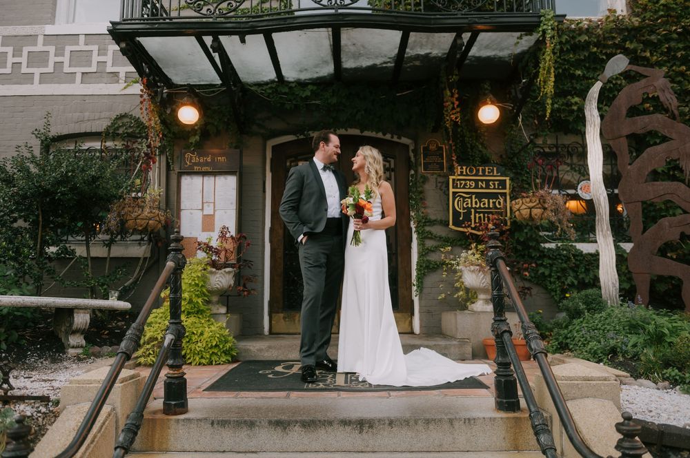Wedding couple posing under rustic outdoor archway with vintage lighting.