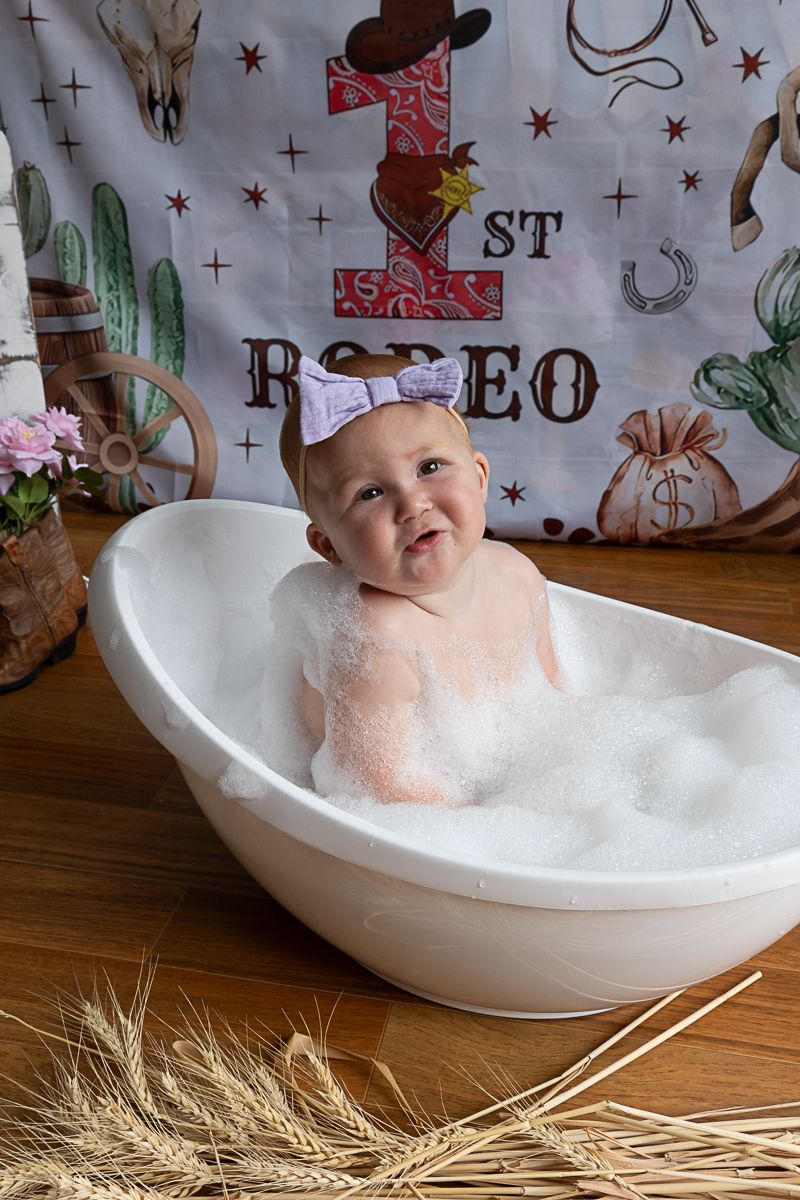 Little girl in a bubble bath at a 1st birthday cowgirl cake smash photo shoot