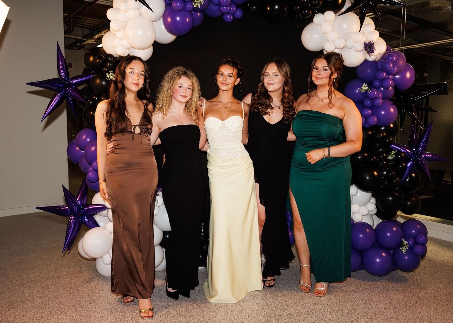 A group of people in formal attire stand together at an event decorated with purple balloons.