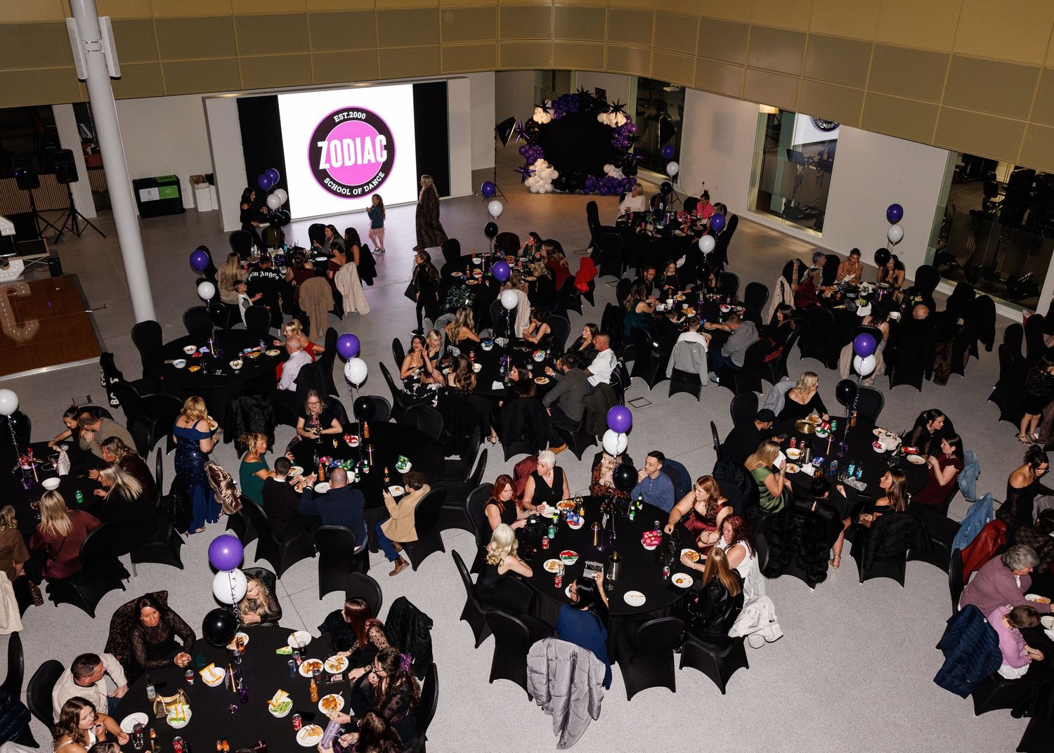 Overhead view of a crowded banquet hall with round tables and purple accent lighting during a formal event.