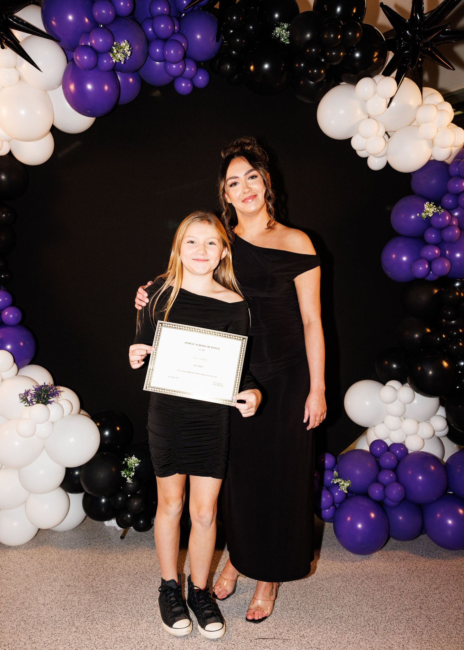 Purple and white balloon arch decorations create an elegant party backdrop against a black wall.