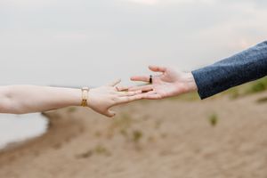 Couple holds hands on sandy beach during romantic outdoor engagement photo session.