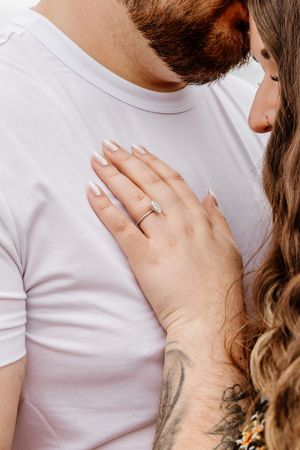 Close-up of woman's hand with diamond engagement ring resting on man's white t-shirt.