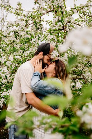 Romantic couple kissing among white flowering apple trees in a lush spring orchard.