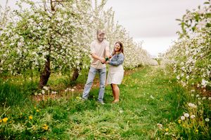 Happy couple dancing and holding hands in a lush blooming apple orchard in spring.