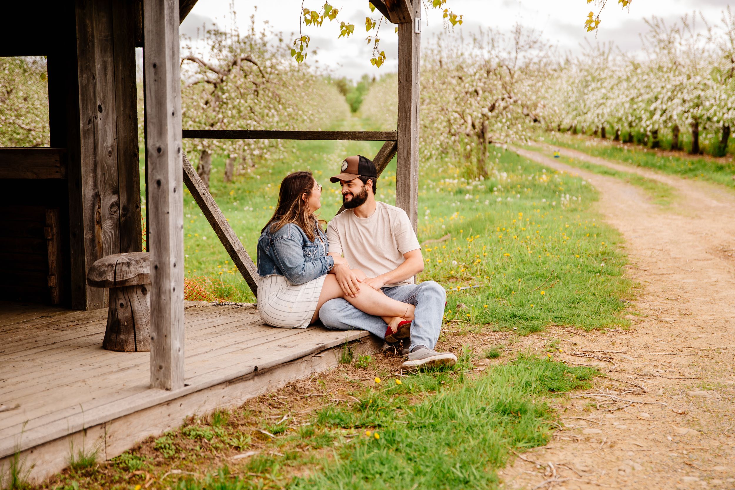Couple sitting together on a rustic wooden porch surrounded by blooming apple orchards in spring.