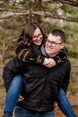 Happy couple laughing as man gives woman a piggyback ride on a woodland trail.