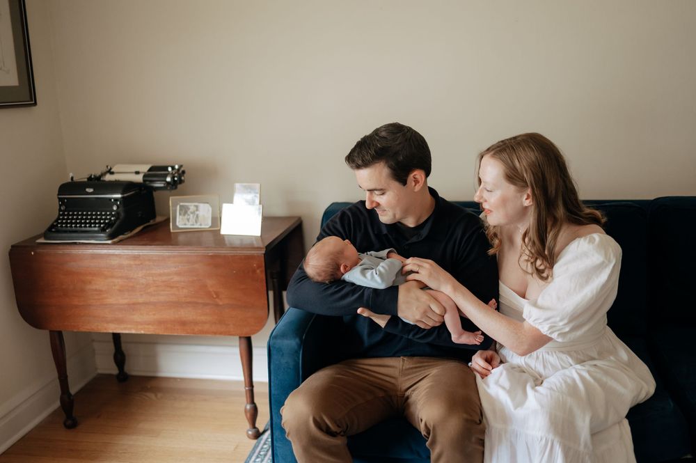 New parents sitting on a couch smiling at their newborn baby in a cozy home setting.
