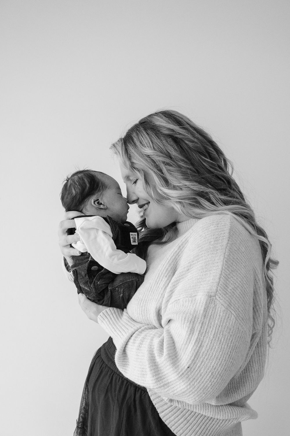 Black and white photo of a mother tenderly touching foreheads with her newborn baby.