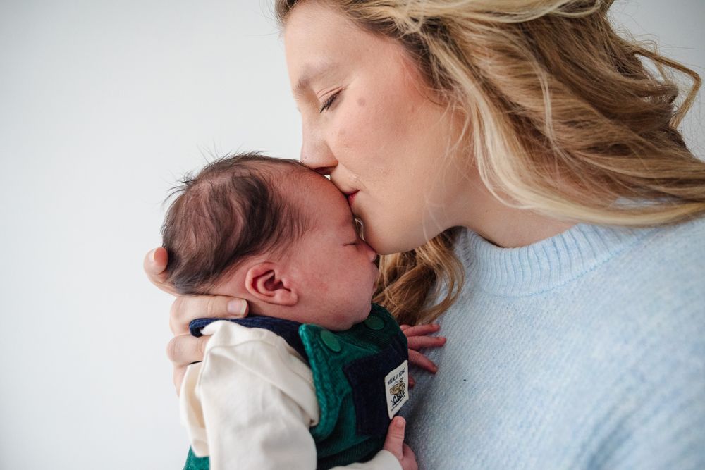 A mother gently kisses her newborn baby on the forehead in a tender moment.
