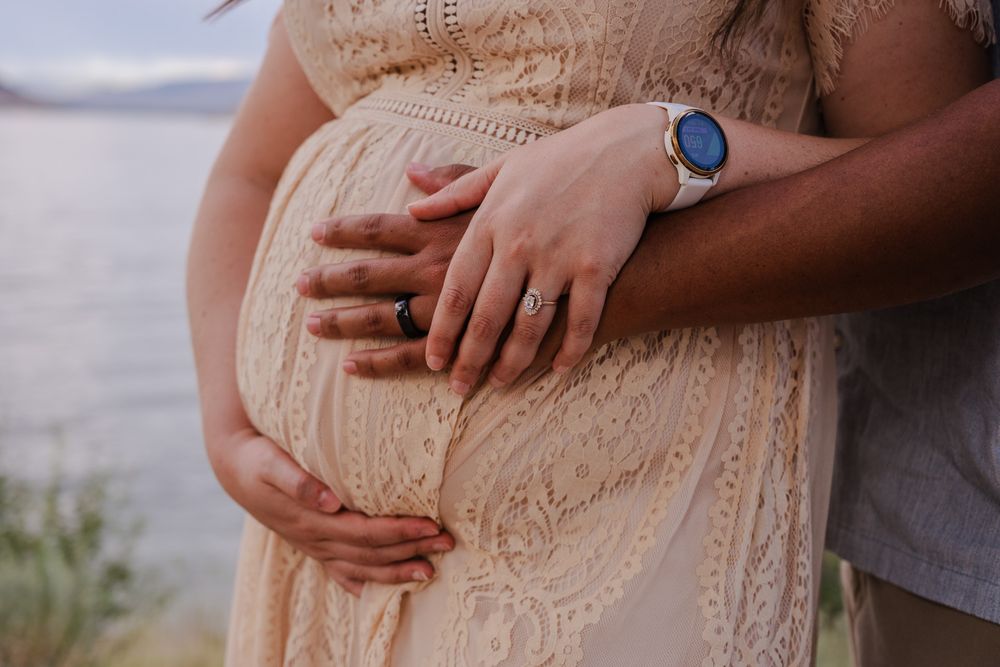 Close-up of couple's hands resting on pregnant belly wearing engagement ring and smartwatch.