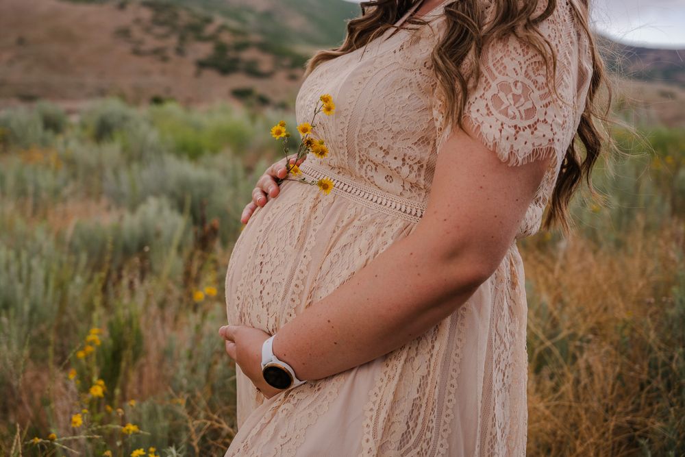 Pregnant woman in lace dress holding wildflowers in a field.