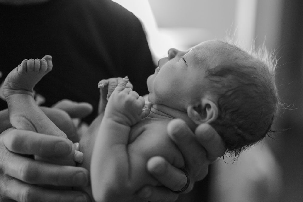 Father cradling tiny newborn baby in both hands in an intimate black and white close-up portrait.