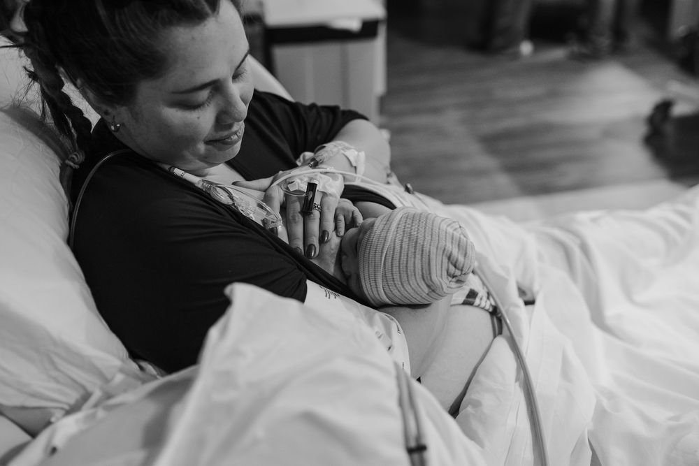 Black and white photo of a new mother smiling while holding her newborn baby in a hospital bed.