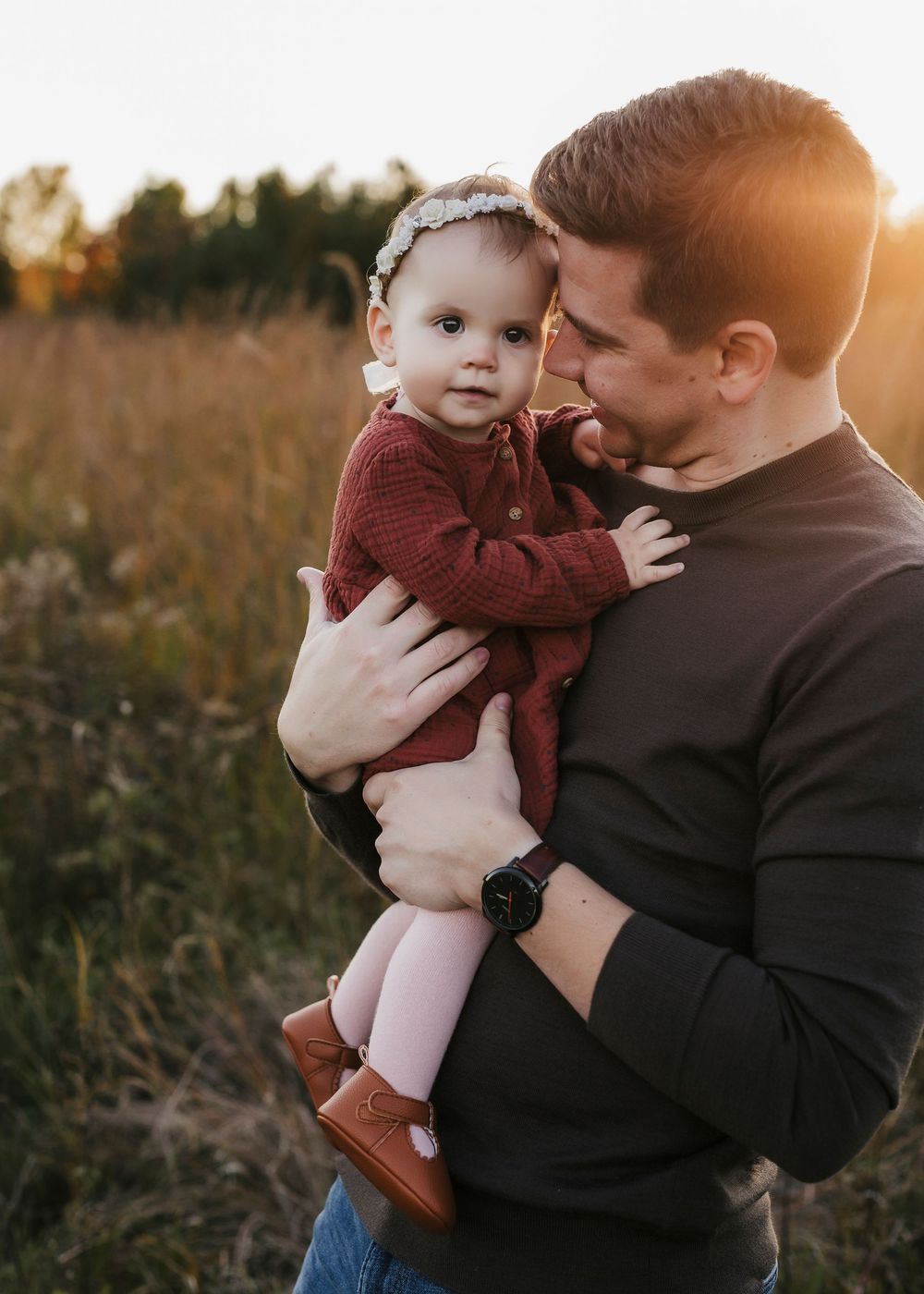 Intimate portrait of a parent and baby against a warm sunset in a rustic field setting.