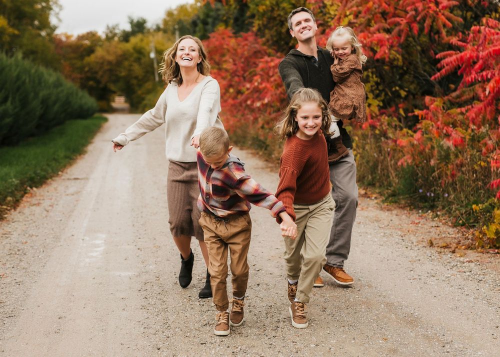 Happy family running and playing on dirt road surrounded by fall colors.