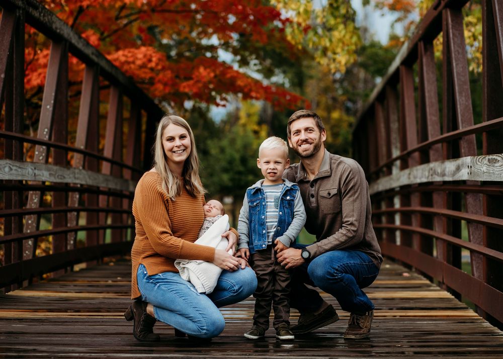 Family sharing tender moments on rustic wooden bridge with autumn foliage.
