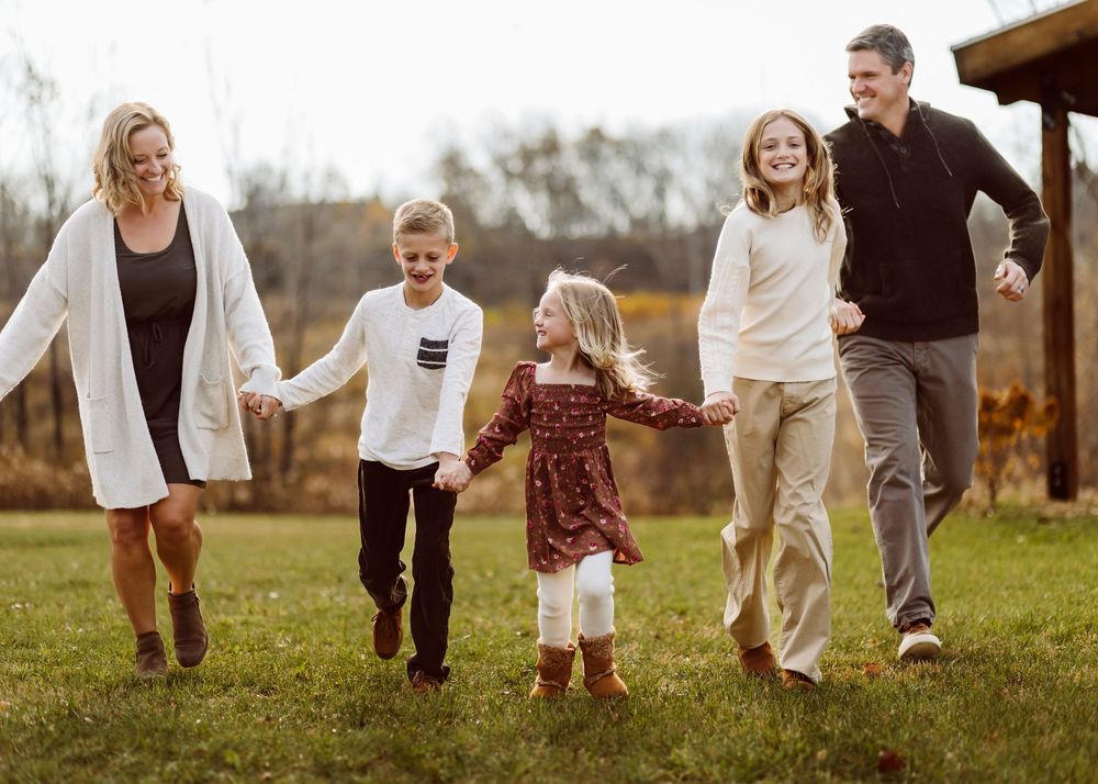 Family playing and running together in a grassy autumn field at sunset.