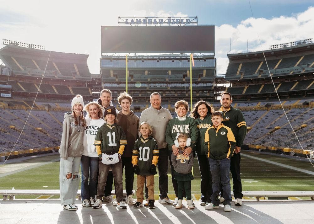 Group photo of fans wearing Green Bay Packers gear at Lambeau Field stadium.