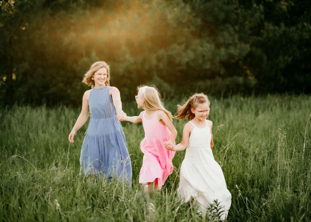 Three figures walk hand in hand through a tall grass meadow at sunset.