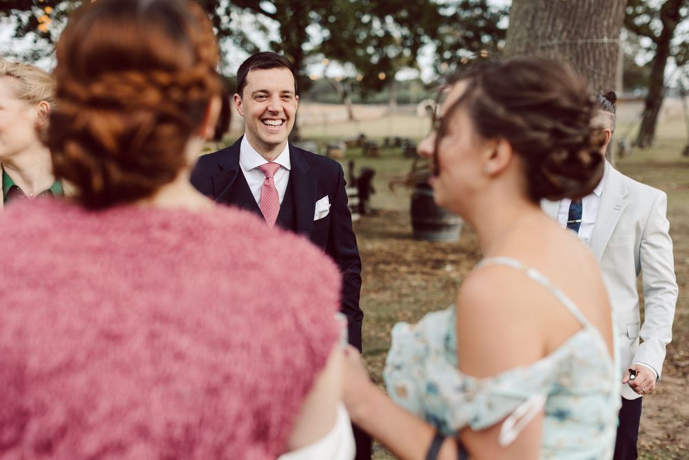 A group of wedding guests in formal attire gather outdoors for a joyful celebration at a rustic venue.