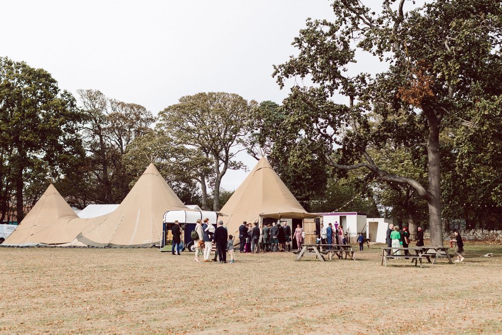 Large tipi-style tents set up for an outdoor event with guests gathering outside.