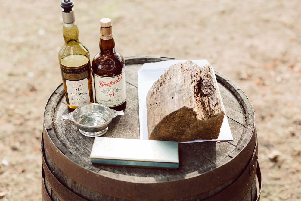 A rustic wooden barrel serves as a table displaying various bottles and items in an outdoor setting.