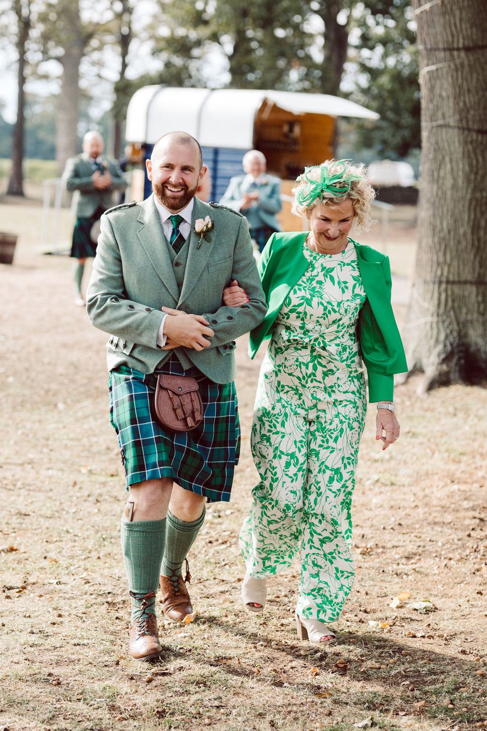 A couple in coordinating green outfits run playfully through a wooded area during a photo session.