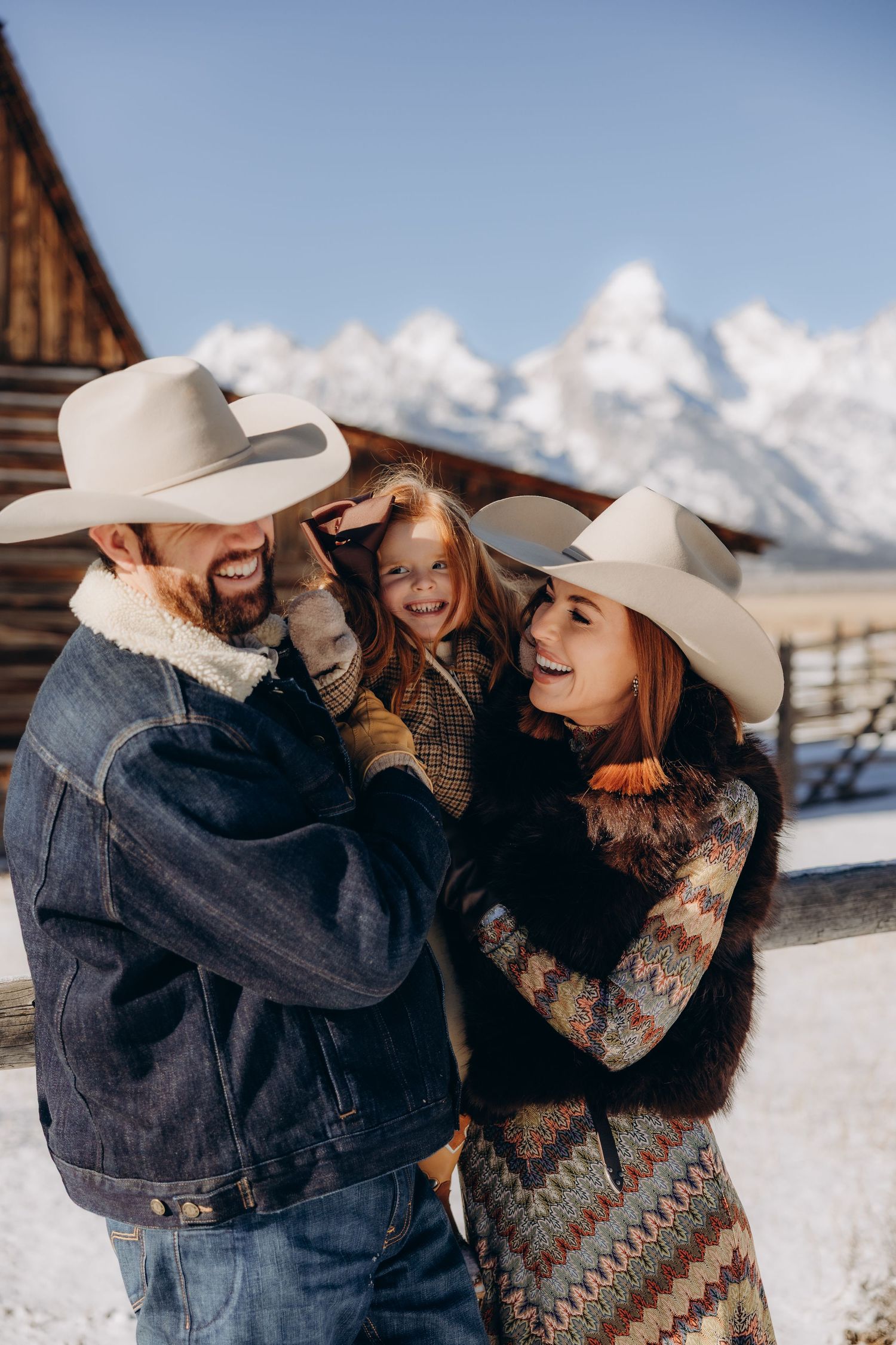 A family in western wear shares a joyful moment together against a snowy mountain backdrop in winter.