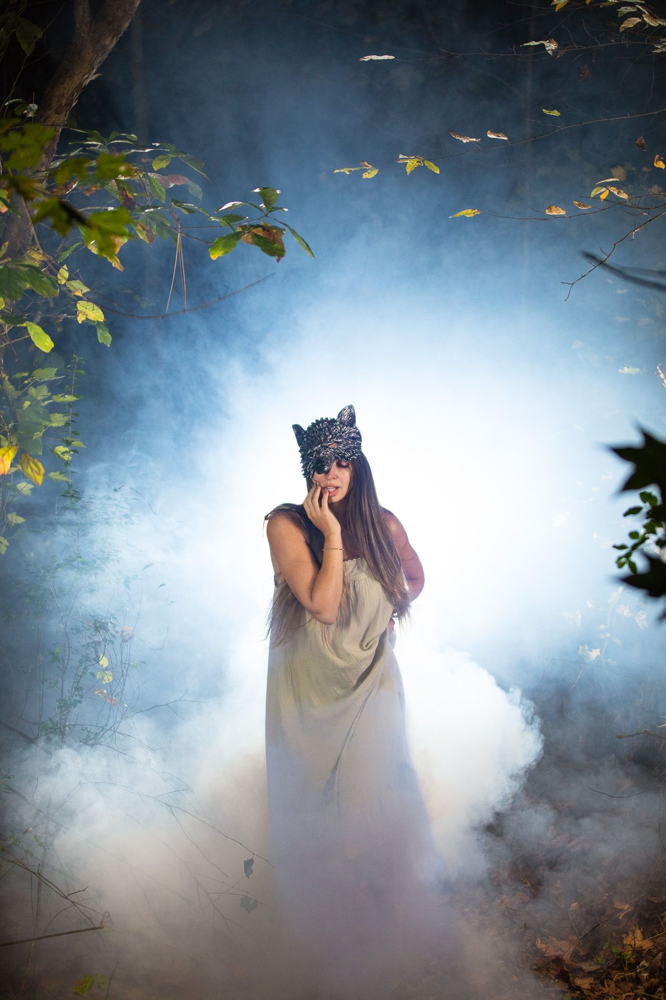 A mysterious woman in a wolf mask emerges through atmospheric fog and leaves in a moody outdoor scene.